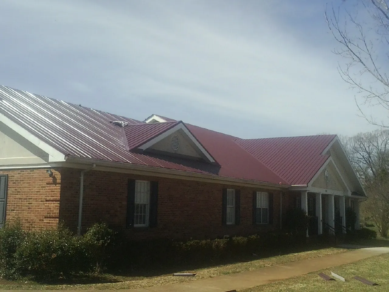 Red metal roof with gabled entries on a long brick building, from a Hail Damage Roof Repair job in Philomath