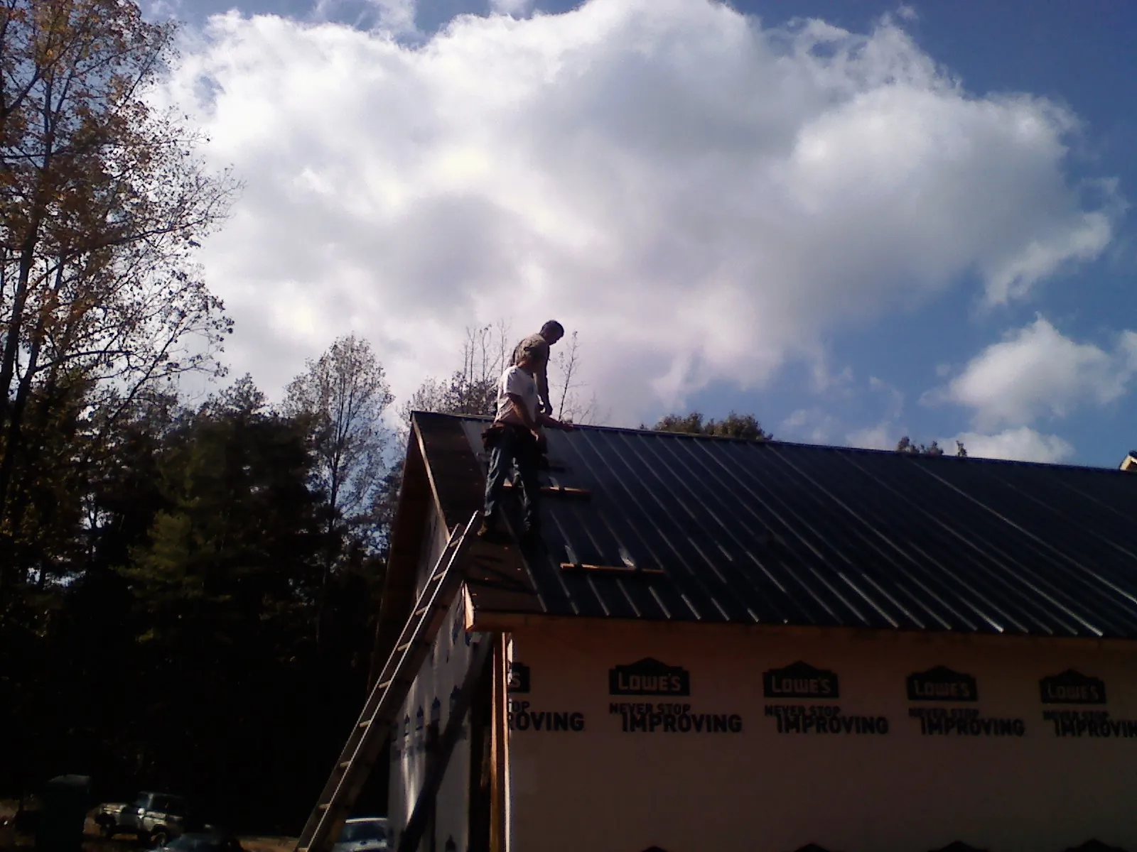 Roofer fastening dark metal panels high against a cloudy sky, from a Roof Inspection job in Philomath